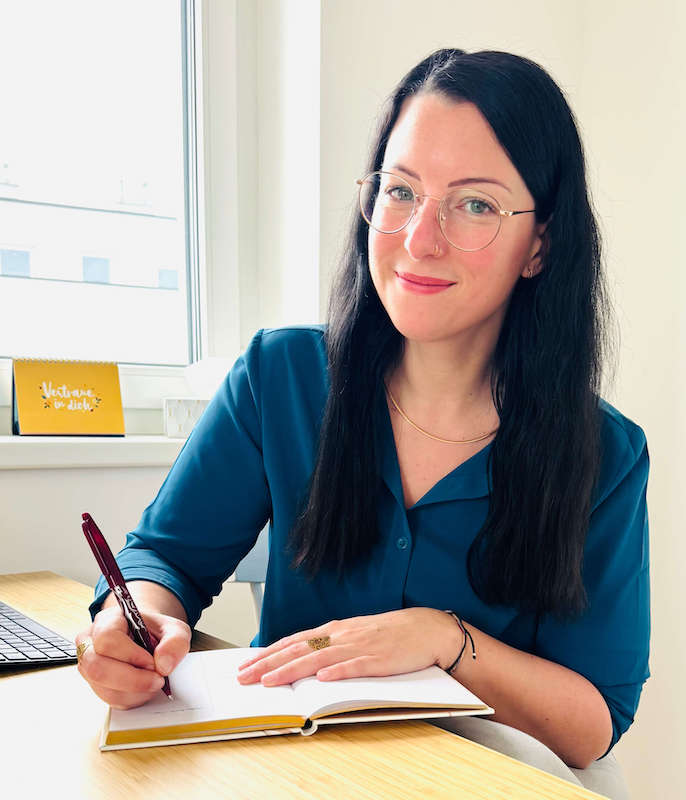 Online-Psychologin Angelika Spies lächelt freundlich in die Kamera, während sie ihre Dokumentation in ein Notizbuch schreibt - bietet professionelle Online-Therapie und Online-Beratung sowie Supervision per Videocall, Audiocall und Chat bei Depressionen, Angst und Panikattacken, geringem Selbstwert und Beziehungsproblemen an - jetzt kostenloses Erstgespräch buchen - Psychologische Online-Beratung & Therapie