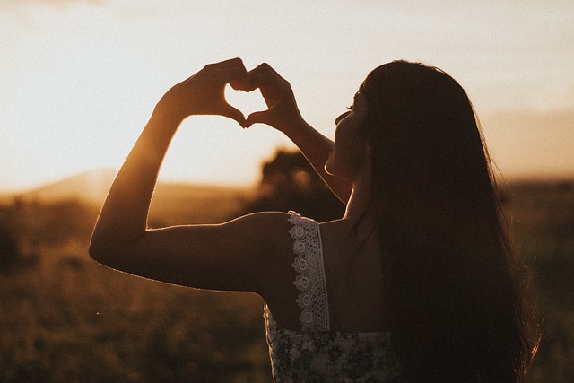 Learning acceptance in therapy - woman forms heart with hands in the sunset - symbol for self-acceptance and inner peace through learning acceptance in therapy